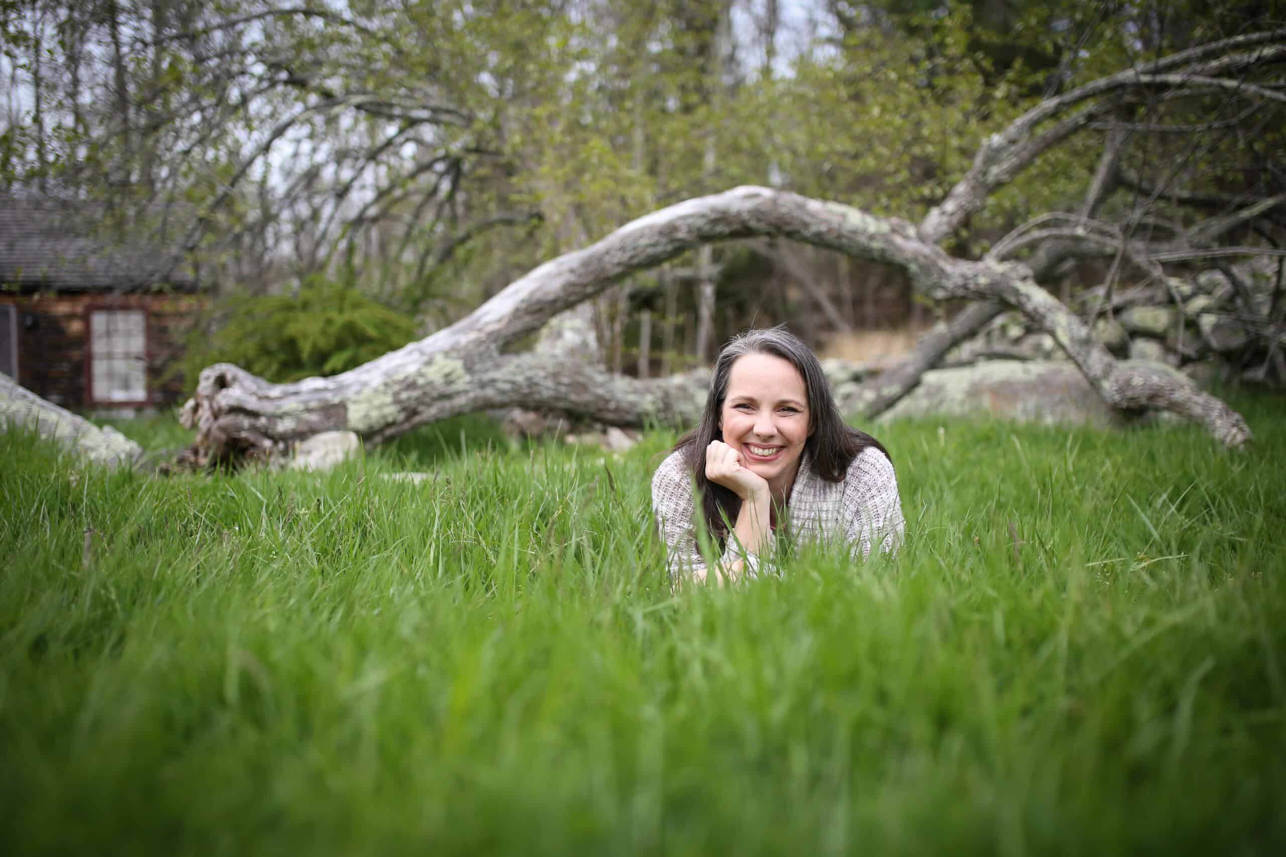 Lynn Turcotte-Schuh lying in a field of grass with a fallen tree in the background